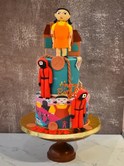 A thrilling two-tier cake based on the popular series Squid Game. It features edible figurines of the guards and the iconic doll, perfect for a fan's birthday party.