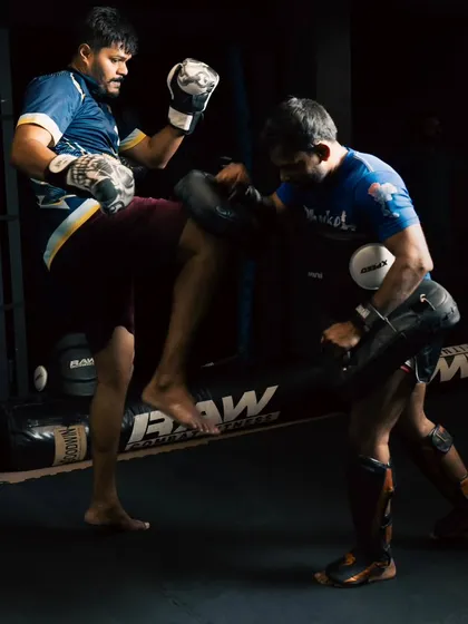Two fighters engage in a pad work drill, with one throwing a kick while the other holds pads, showing a typical training scenario.