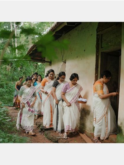 The women in traditional attire entering a rustic, traditional house, a glimpse into authentic Kerala culture.