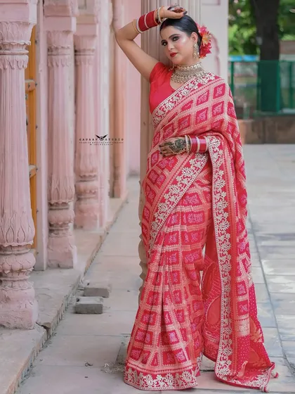 A stylish full-length pose against a pink pillar, showcasing the vibrant red saree.