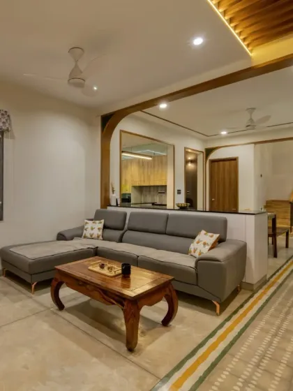 An open-plan living space designed for connection and calm. We crafted the custom grey sectional sofa and the solid wood coffee table to anchor the room, while wooden arches create a seamless flow into the dining area, embodying our warm minimalist approach.
