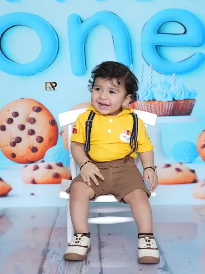 A happy baby boy smiles for the camera in the cookie-themed setup. The "ONE" sign and cheerful colors make this a perfect first birthday portrait.