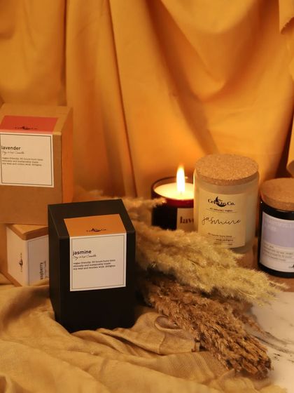 This shot displays the scented candles along with their packaging. The warm, ambient light from a lit candle creates a gentle and inviting mood, showing customers the complete product experience from box to use.