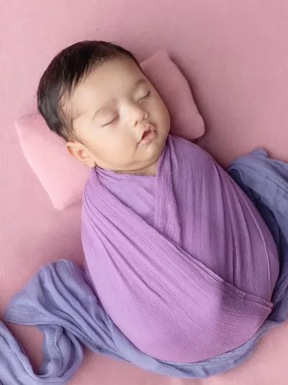 The flowing fabric of the wrap adds a beautiful artistic element to this newborn photo.
