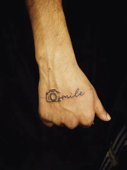 A clever design that combines a camera outline with the word "smile." This is a great example of a personalized, minimalist tattoo that reflects a hobby or passion.