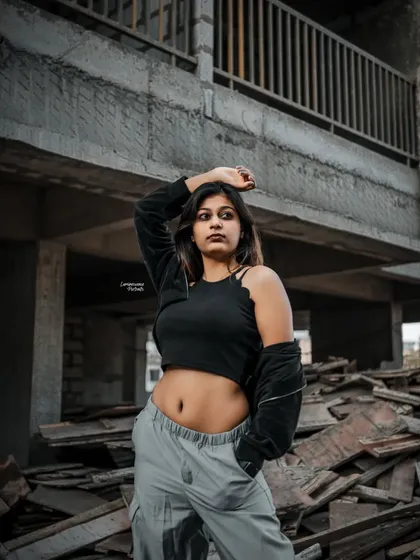 A strong pose with the model's hand on her head, her crop top and cargo pants contrasting with the unfinished concrete building behind her.