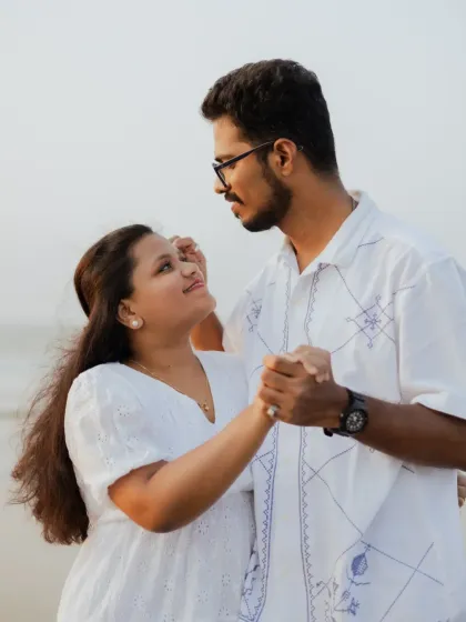 A sweet, dance-like pose between the couple during their beach photoshoot. These playful moments showcase their happy connection.