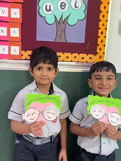 Students hold up the heart-shaped cards they made, featuring cute illustrations of grandparents.
