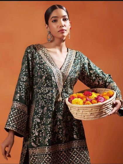 A model holds a basket of flowers while wearing a deep green brocade kurta with intricate gold and silver weaving, perfect for a festive puja.