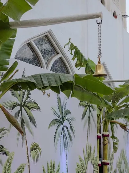 We used custom-printed wallpaper with a Pichwai-inspired palm motif to cover the walls, blending seamlessly with the real banana trees used in the decor. This created a lush, cohesive, and immersive environment.