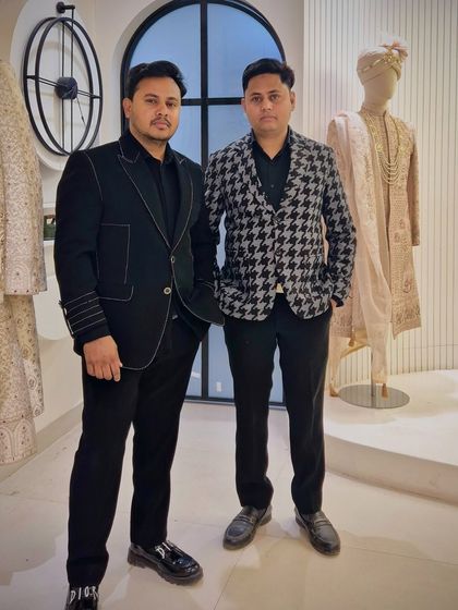 The designer with a client, both in custom jackets. The client wears a black jacket with white contrast stitching, while the designer is in a houndstooth pattern blazer.