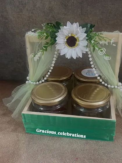 This green wooden tray hamper is decorated with a sunflower theme. It holds four jars that can be filled with a variety of eatables, making it a substantial and beautiful return gift.