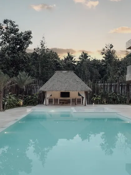 The swimming pool reflects the sky and surrounding trees, acting as a tranquil centerpiece for the property. The design integrates the pool with the home's foundation, making it feel like a natural extension of the living space.
