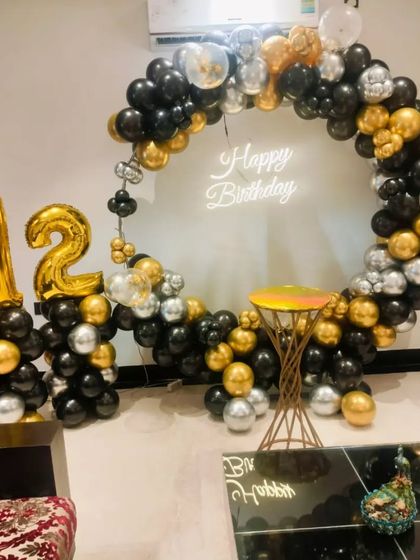 A sophisticated black, gold, and silver theme for a 12th birthday. This setup features a circular balloon arch, a neon sign, and large '12' foil balloons.