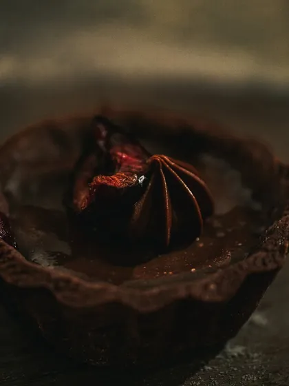 A macro shot of a chocolate tart, focusing on the rich texture of the ganache and the delicate pastry. Dark lighting enhances the decadent feel.