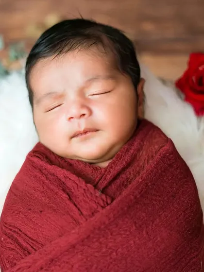 A precious newborn boy wrapped in red, sleeping among roses. This classic and beautiful setup creates a timeless and heartfelt memory.