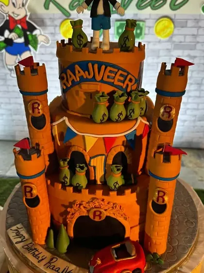 A grand castle cake for a Richie Rich-themed party. This orange castle is decorated with edible money bags and a character topper.