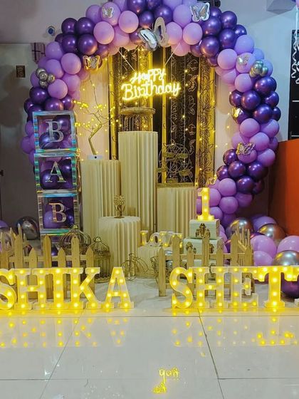A beautiful and elaborate setup designed for a home celebration. This decor features a full circular balloon arch in purple and gold, a neon sign, and large marquee letters, showing how I can create a grand look in an intimate space.
