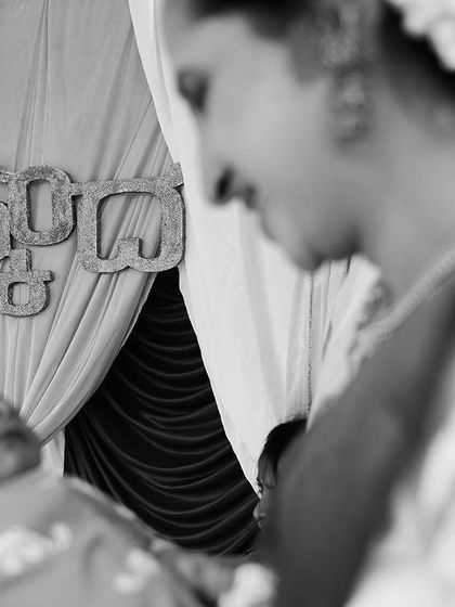 A mother's gentle smile as she looks down at her newborn. This intimate black and white close-up, taken during a naming ceremony, freezes a moment of pure maternal love.