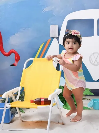 Ready to catch a wave. This little one is standing tall in our beach-themed setup. The props, like the mini surfboard and cooler, add a fun, playful touch to the scene.