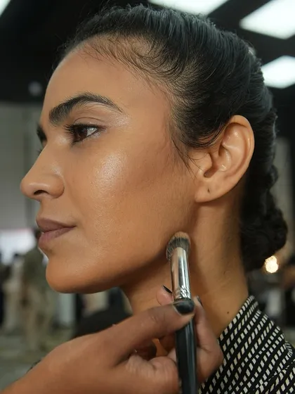An artist uses a brush to blend foundation seamlessly on a model's jawline. Flawless skin is the canvas for every great makeup look.