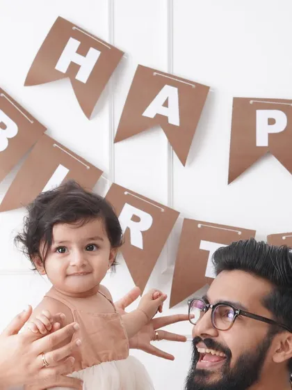 A candid close-up of a family during a birthday shoot, capturing a moment of laughter between the father and his baby girl.