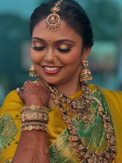 A close-up of Prithivi's second Muhurtham look. The bright yellow and green saree is paired with a stunning gold eyeshadow and a warm smile, showing a versatile traditional style.