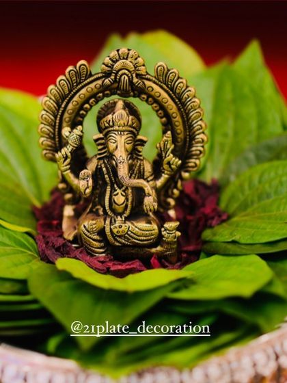 A close-up of a beautiful brass Ganesha idol placed on a bed of fresh betel leaves and flowers. This is a classic element I use in my plate arrangements for an auspicious start.