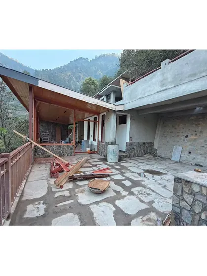 The homestay nearing completion, showing the relationship between the covered wooden veranda and the open stone-paved terrace. The structure is built to follow the contours of the hillside.
