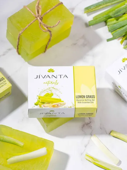 A bright, fresh flat lay of Jivanta Naturals' Lemon Grass soap on a marble background. The styling with fresh lemongrass stalks highlights the product's main ingredient and scent.
