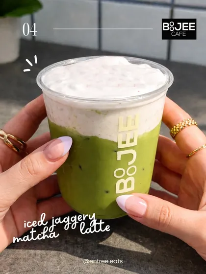 A handheld shot of an Iced Jaggery Matcha Latte. This personal perspective makes the drink feel accessible and desirable. The two toned layers of the drink are clearly visible, making it look delicious.