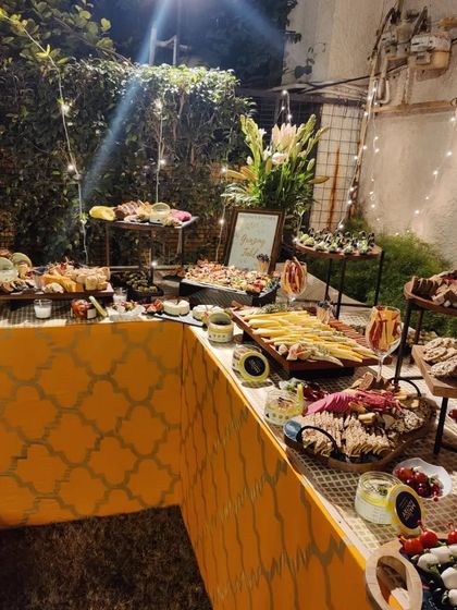 A beautiful outdoor grazing table setup for a Diwali party. The yellow table runner and string lights create a festive and warm ambiance for guests to enjoy the food.