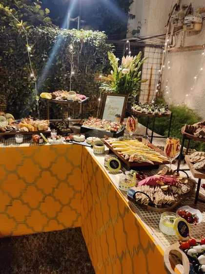 An outdoor grazing table illuminated by fairy lights for a Diwali party. The setup includes a butter board, prawn cocktails, and various crackers and dips, creating a magical evening ambiance.