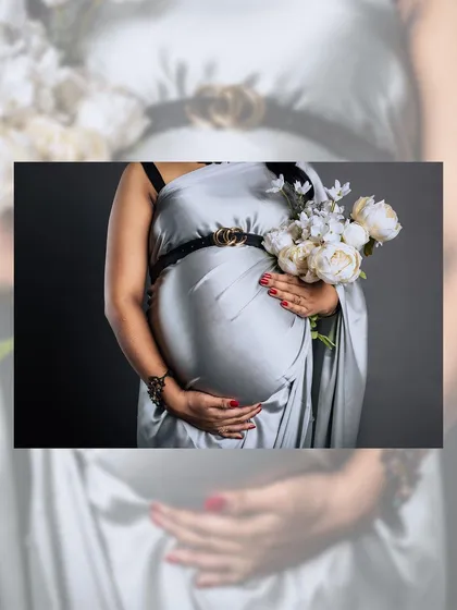 A detailed shot focusing on the baby bump, draped in a shimmering silver saree and adorned with a stylish belt. The mother's hands gently cradle her belly, a classic gesture of maternal love.