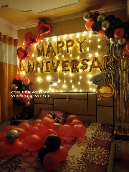 A classic anniversary surprise that never fails to impress. This bedroom decoration features "Happy Anniversary" foil balloons against a wall of fairy lights, a festive mix of red, black, and silver balloons, and a special diamond ring balloon to mark the occasion.