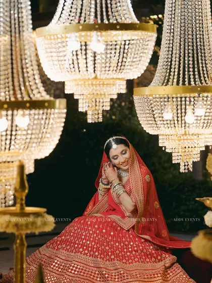 A shy, beautiful smile from the bride as she adjusts her earring, surrounded by the dazzling light of multiple crystal chandeliers.