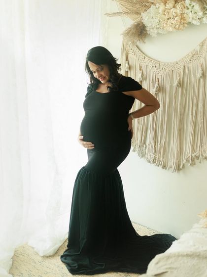A gorgeous portrait of a mama-to-be in a classic black mermaid-style gown. The soft window light and boho-chic studio setup create a beautiful, dreamy atmosphere.