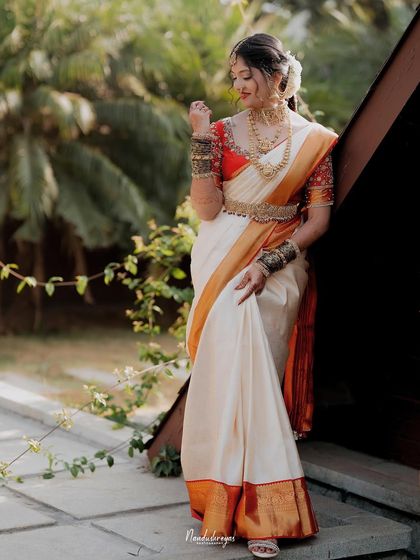 A full-length portrait of the bride in her stunning white and orange silk saree. Her pose exudes confidence and grace.