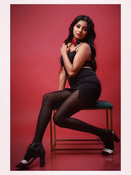 A full-length shot of a model in a glamorous black outfit against a red background. The pose is strong and confident, creating a striking fashion image.