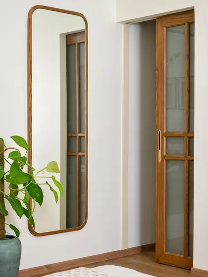 A custom wood-framed mirror with rounded corners complements the sliding wooden door of this wardrobe, adding a soft, organic touch to the entryway.