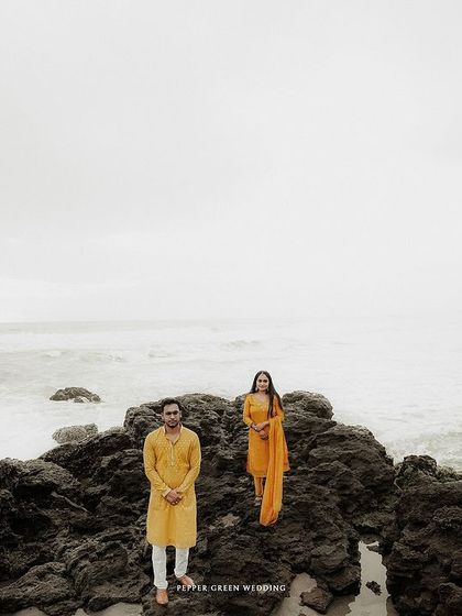A wide shot of Aiswarya and Vishnu against the vast ocean, with their yellow outfits providing a pop of color. This kind of shot emphasizes the epic scale of both nature and their love.