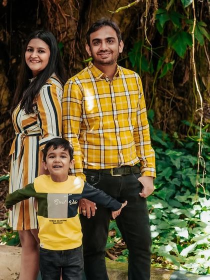 A family of three posing in a lush, green park. The coordinated yellow and striped outfits add a bright and cheerful touch to their outdoor portrait.