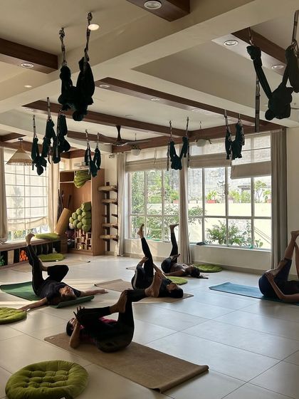 Students lie on their backs in a gentle stretching pose, finding release and relaxation. The natural light from the windows enhances the peaceful atmosphere.