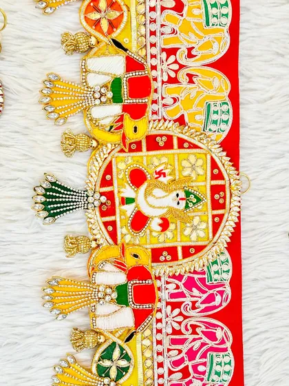A close-up of a Ganesha and elephant themed bandhanwar. The bright red color and traditional motifs make it an auspicious decoration for your main gate this Diwali.
