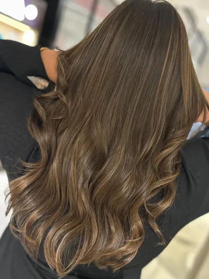 A warm caramel balayage blend that looks incredibly rich and glossy. The long layers haircut and soft waves create a glamorous and healthy-looking style.