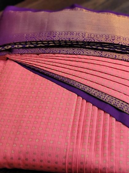 A pre-pleated client saree in a vibrant coral pink, neatly box-folded.