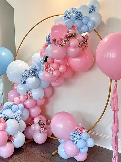 A lovely gender reveal or baby shower setup. The gold ring is adorned with pink and blue balloons and delicate floral accents, creating a beautiful and balanced design.