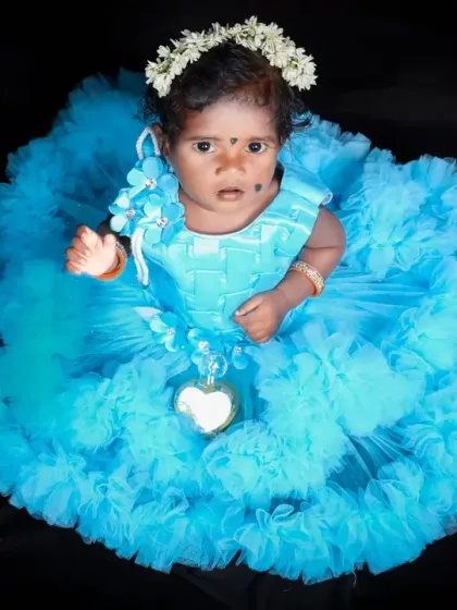 An overhead shot of a baby girl in a stunning, ruffled blue dress. This angle showcases the beautiful design of the dress, making her look like a little flower blooming.