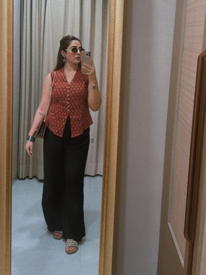 This mirror selfie showcases a balanced silhouette with a fitted waistcoat and flowy wide-leg pants. The V-neckline and vertical buttons create a slimming effect, making it a smart and stylish Indo-Western look.