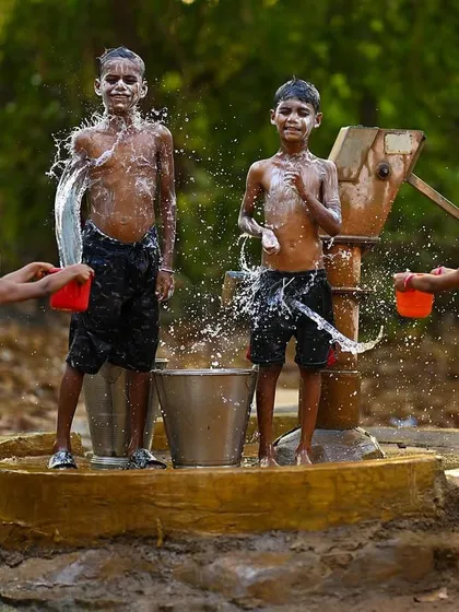 Two boys stand proudly after being splashed, while two girls prepare the next wave of water. This posed moment amidst the action shows their playful and confident spirit.